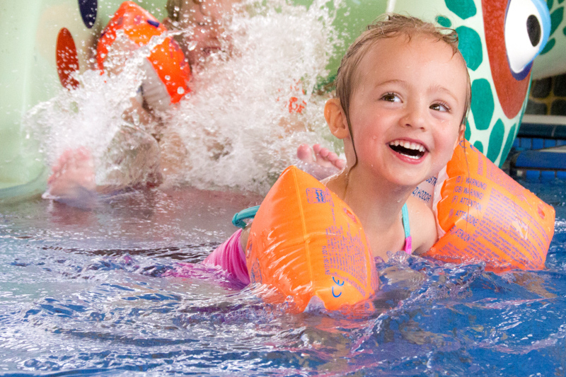 Junges lachendes Mädchen mit Schwimmflügeln in einem Schwimmbecken